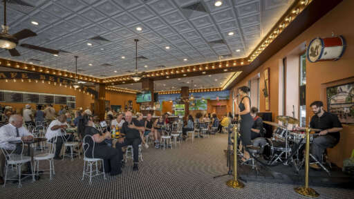 Live music at Cafe Beignet Sheraton. A singer, drummer, and guitarist perform onstage as guests eat and chat.