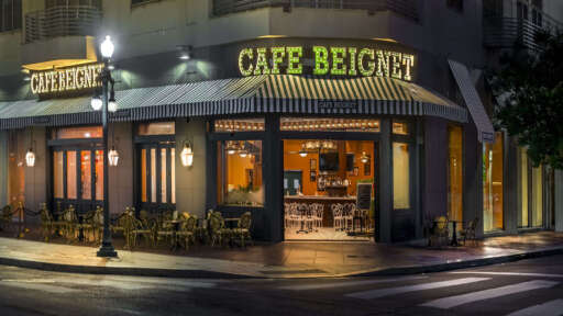 The exterior of Cafe Beignet Sheraton at night, glowing on a rainy evening.
