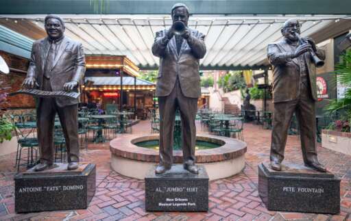 Three statues in New Orleans Musical Legends Park with Cafe Beignet in the background.
